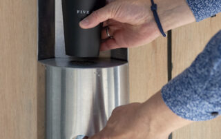 Hände bedienen einen Wasserspender